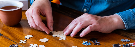 Close-up of an elderly woman's hands solving a jigsaw puzzle, wide banner