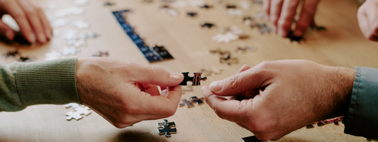 Middle-aged man and woman sorting jigsaw puzzle pieces together at a table, wide banner